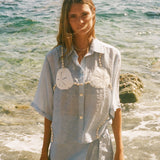 Image of woman in light blue sand dollar bikini shirt, standing ankle deep in the ocean, with a matching skirt underneath.