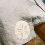 Close cropped image of a light blue skirt featuring an appliquéd sand dollar.