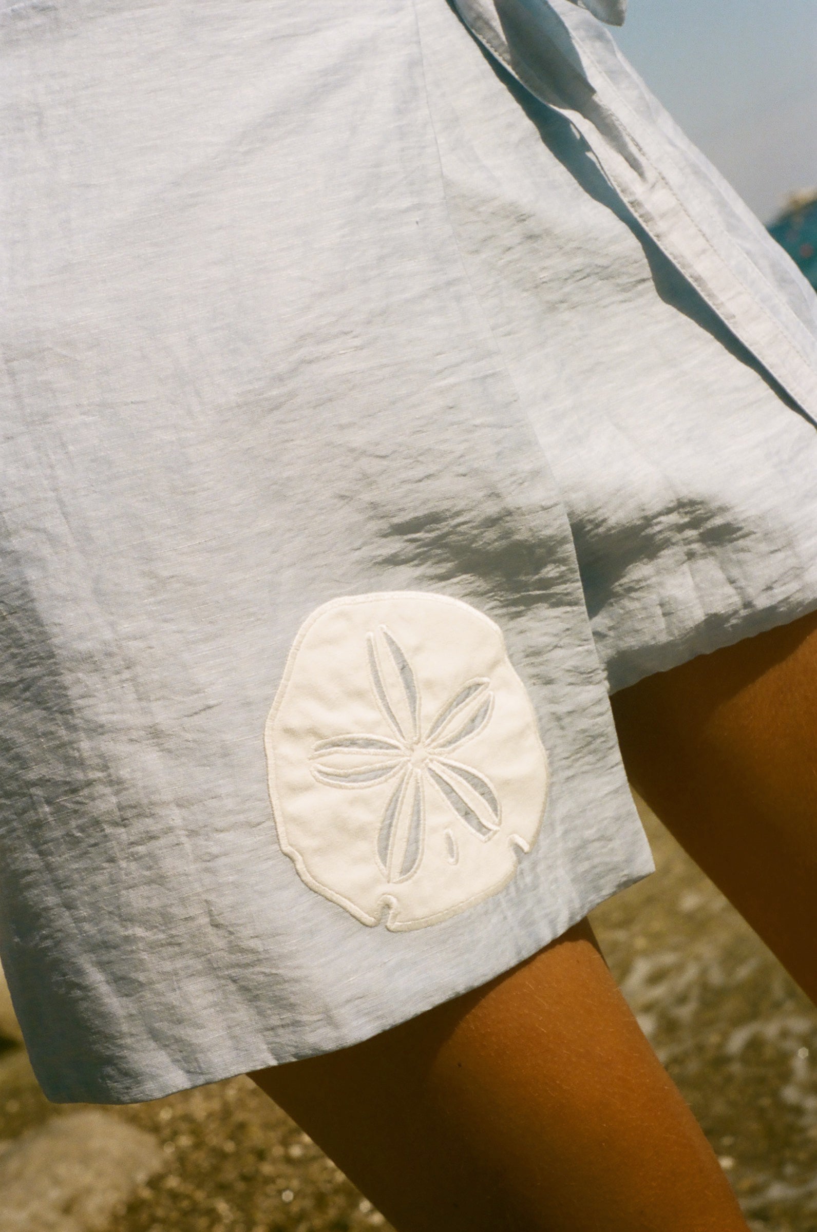 Close cropped image of a light blue skirt featuring an appliquéd sand dollar.