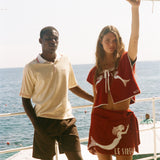 Two people wearing Le Sirenuse x Tombolo pieces, standing in front of the ocean. 