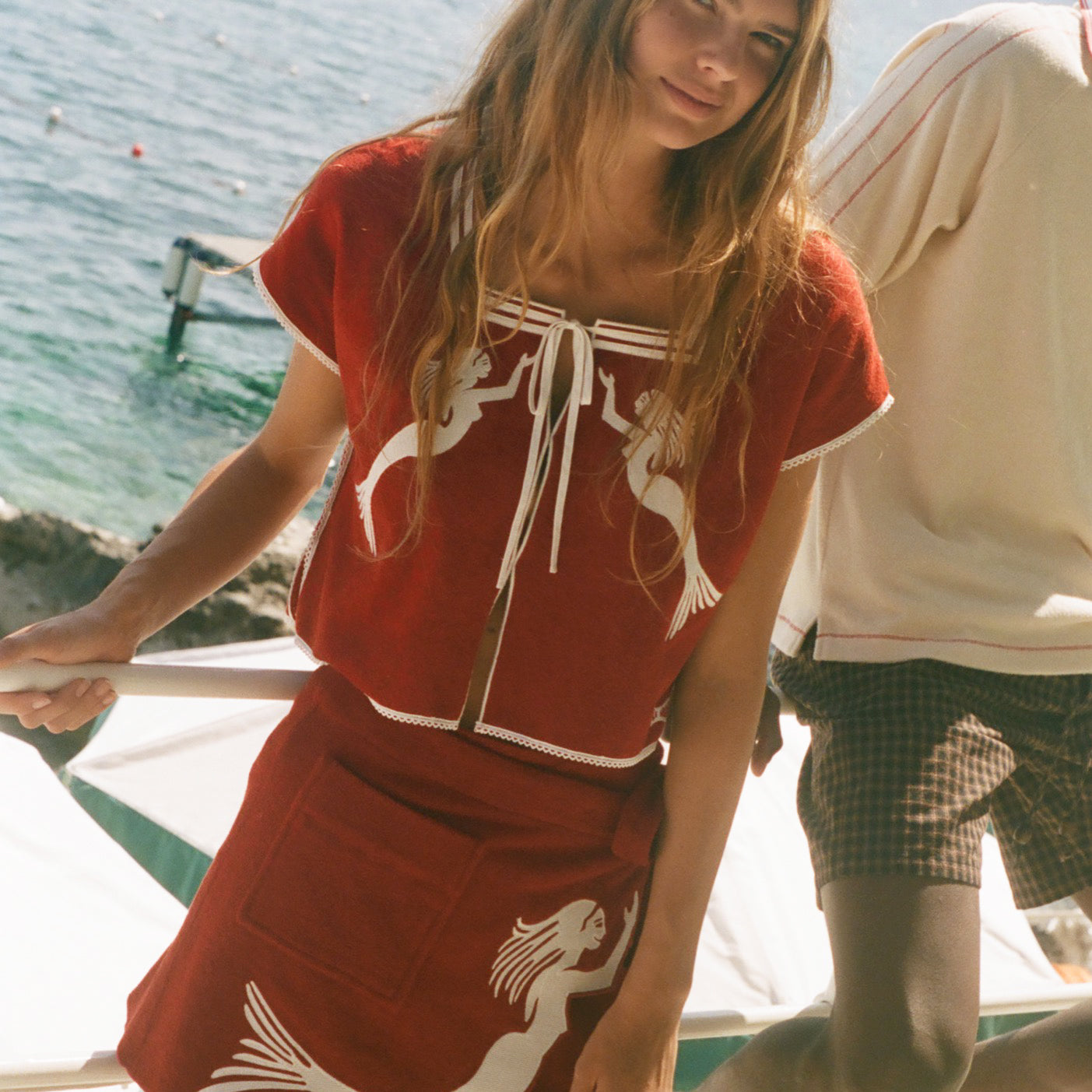 Woman wearing matching Le Sirenuse hand towel set, standing in front of the ocean. 