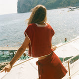 Person in a red Le Sirenuse outfit standing on a boat looking at a scenic view of water and cliffs.