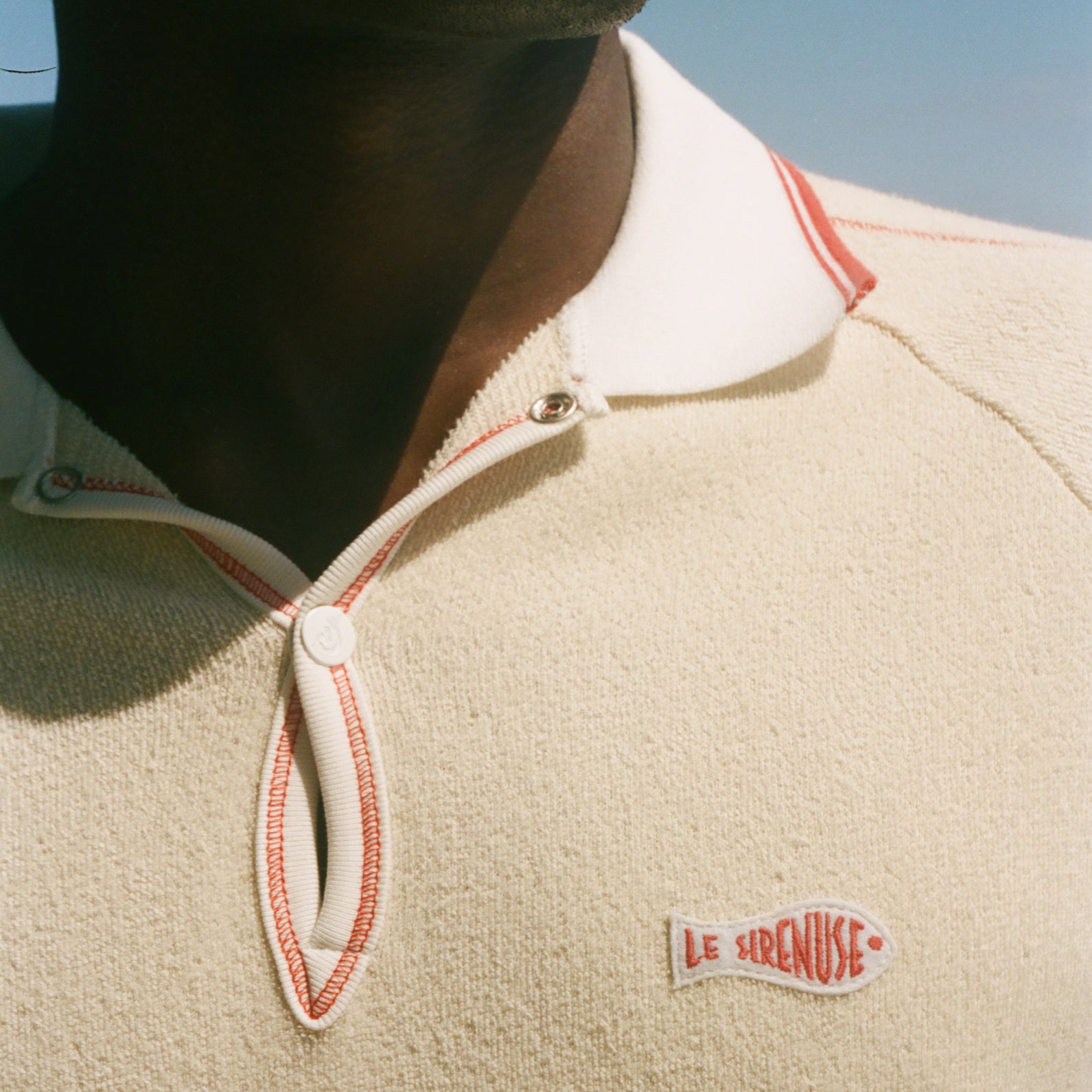 Close-up of a person wearing a beige polo with a Le Sirenuse patch. 