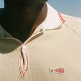 Close-up of a person wearing a beige polo with a Le Sirenuse patch. 