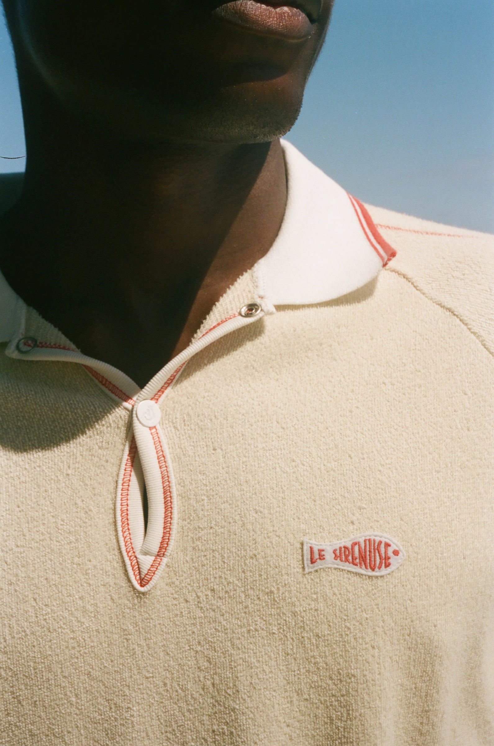 Close-up of a person wearing a beige polo with a Le Sirenuse patch. 