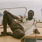 Man sitting on a boat with scenic background, wearing Le Sirenuse all-over patterned shirt. 