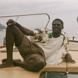 Man sitting on a boat with scenic background, wearing Le Sirenuse all-over patterned shirt. 