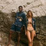 Two people wearing matching blue outfits with gold embroidery on a rocky surface.
