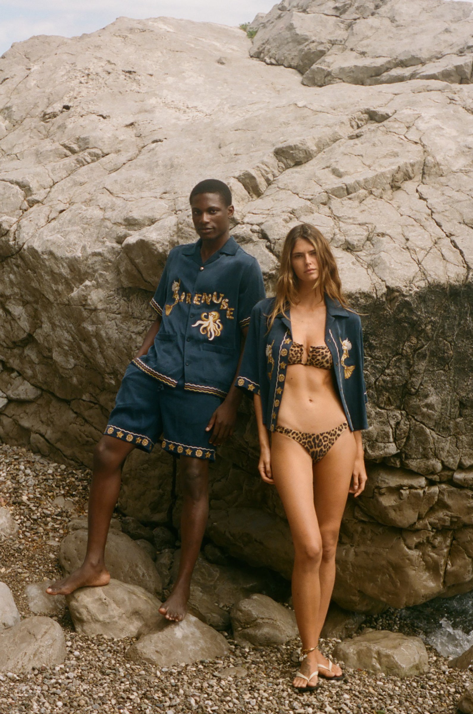 Two people wearing matching blue outfits with gold embroidery on a rocky surface.