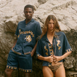 Two people wearing matching blue outfits with gold embroidery on a rocky surface.