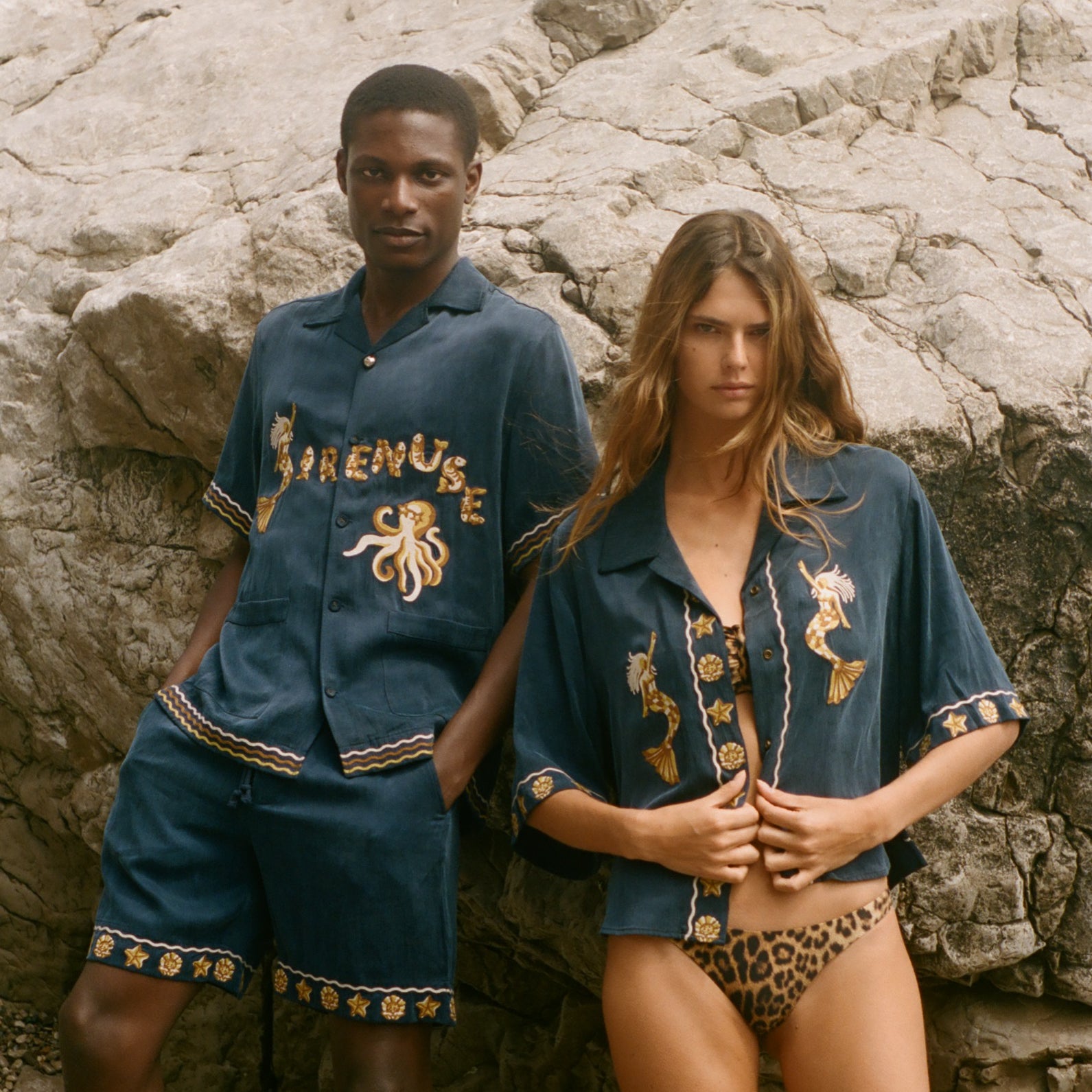 Two people wearing matching blue outfits with gold embroidery on a rocky surface.