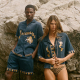 Two people wearing matching blue outfits with gold embroidery on a rocky surface.