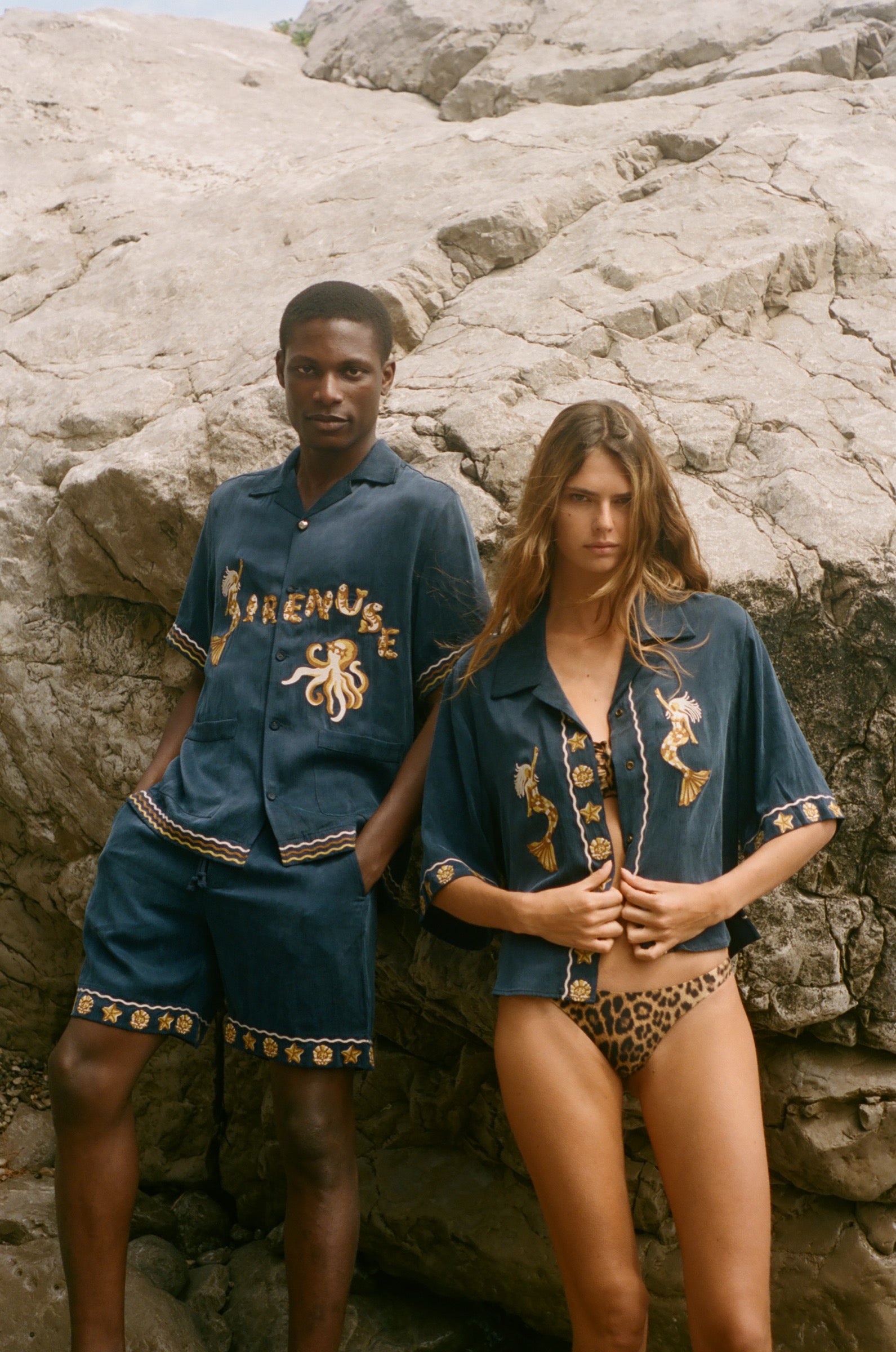 Two people wearing matching blue outfits with gold embroidery on a rocky surface.
