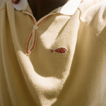 Close-up of a person wearing a beige polo with a Le Sirenuse patch. 