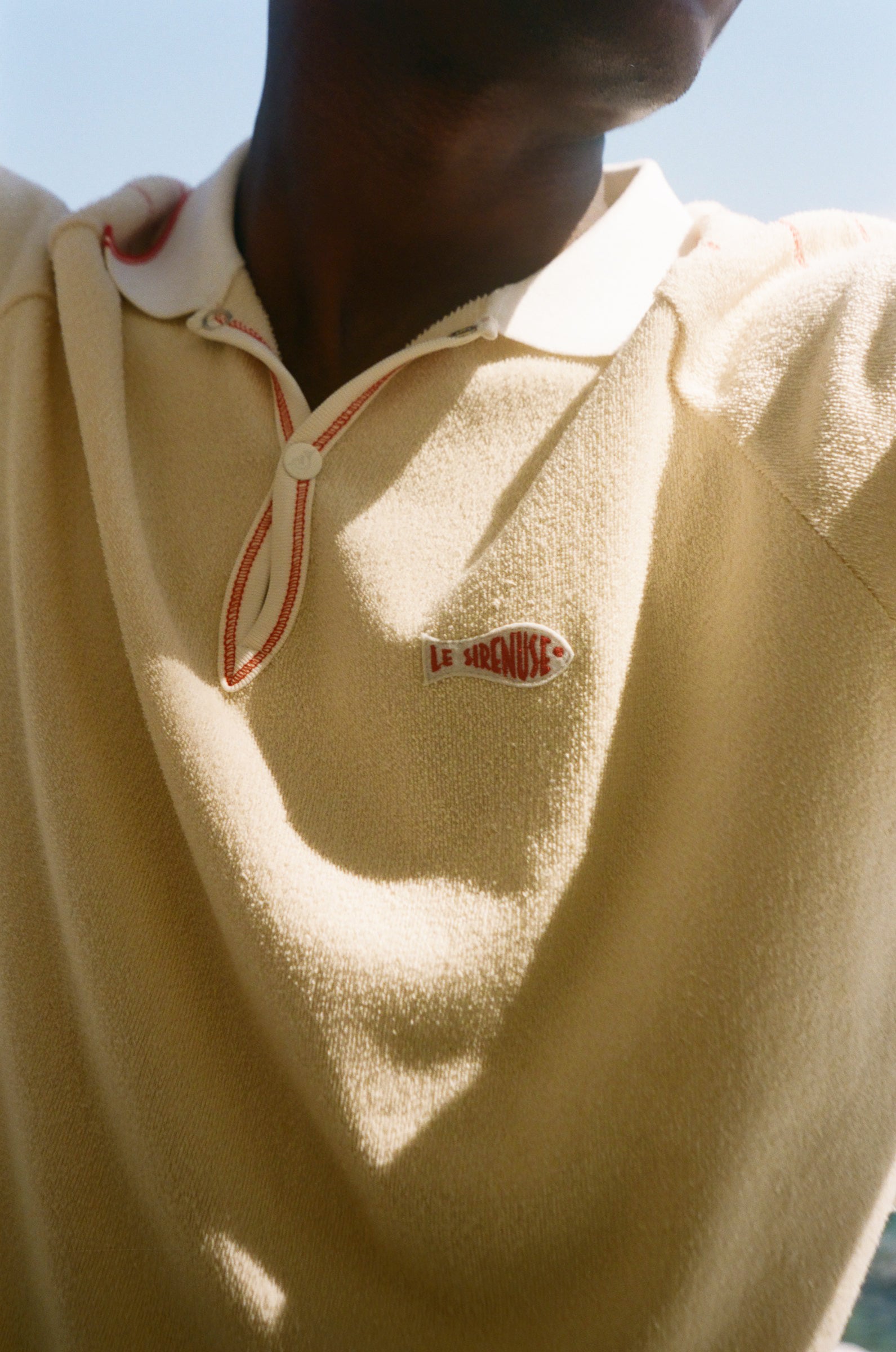 Close-up of a person wearing a beige polo with a Le Sirenuse patch. 
