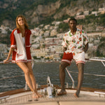 Two people on a boat with scenic mountains in the background, wearing items from the Le Sirenuse x Tombolo collection.