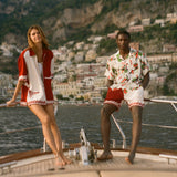 Two people on a boat with scenic mountains in the background, wearing items from the Le Sirenuse x Tombolo collection.