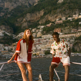 Two people standing on a boat with a scenic view of a coastal town and mountains in the background.