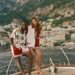 Two people standing on a boat with a scenic view of a coastal town and mountains in the background.