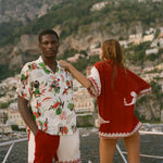 Two people standing on a boat with a scenic view of a coastal town and mountains in the background.