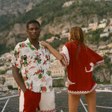 Two people standing on a boat with a scenic view of a coastal town and mountains in the background.