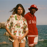 Two people standing in front of the beach, wearing Le Sirenuse x Tombolo collection items. 