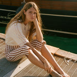 Woman sitting on a dock by a boat, wearing the Le Sirenuse polo shirt.