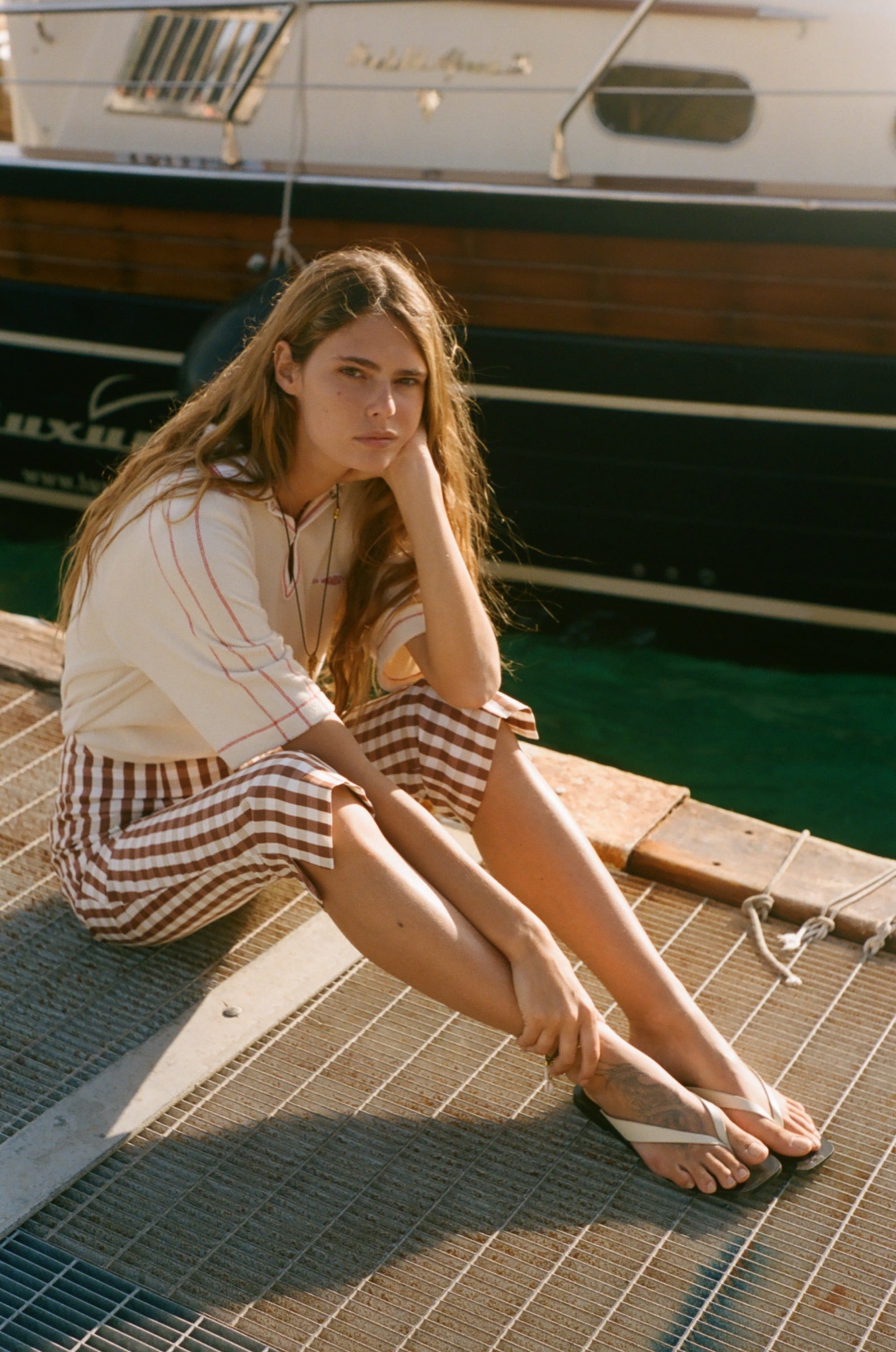 Woman sitting on a dock by a boat, wearing the Le Sirenuse polo shirt.