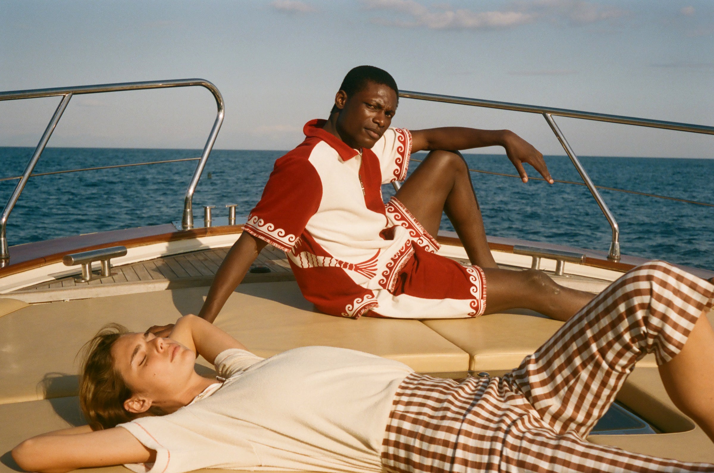 Two people on a boat with one person lying down and the other sitting, wearing the Le Sirenuse x Tombolo collection.