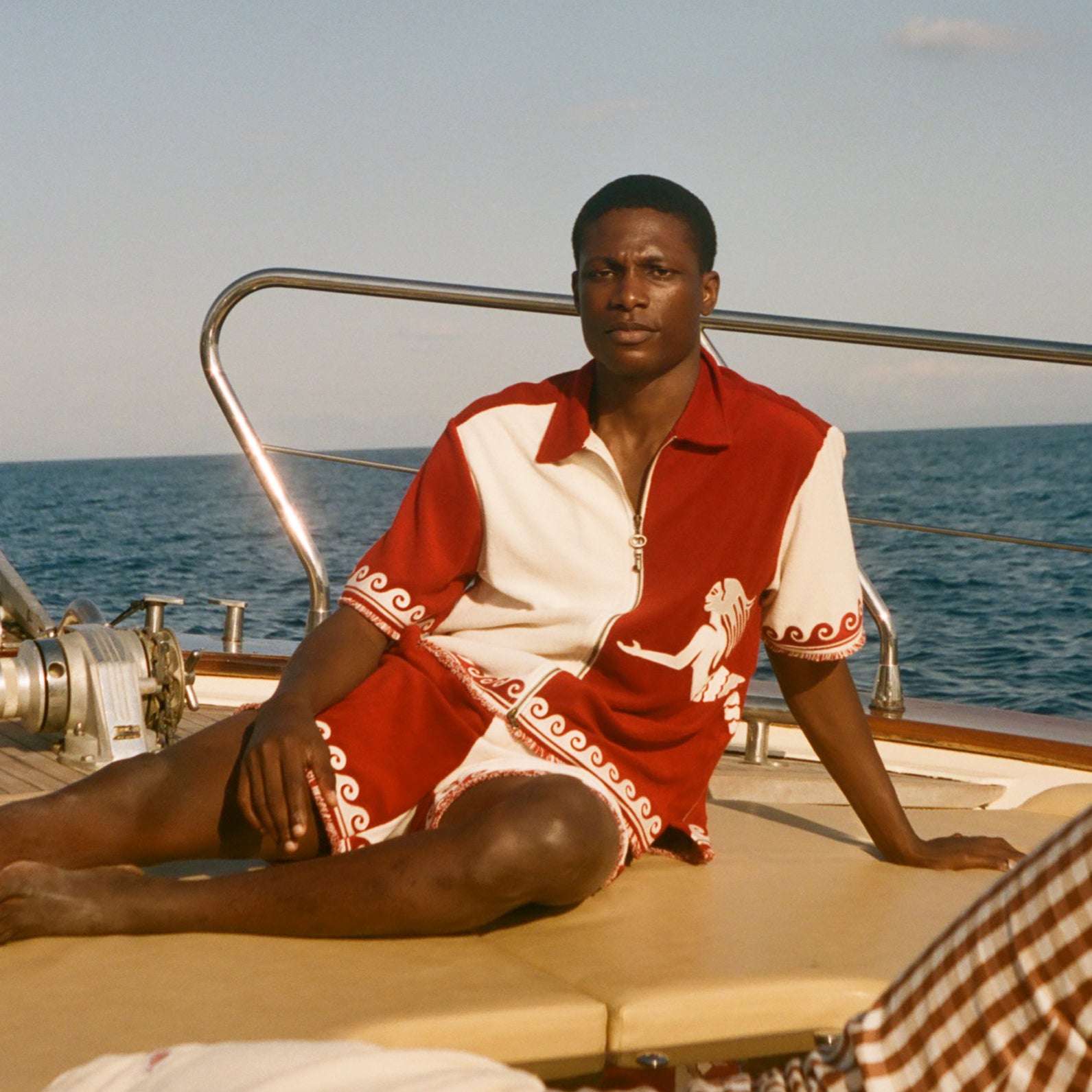 Person sitting on a boat wearing a red and white outfit with ocean and sky in the background