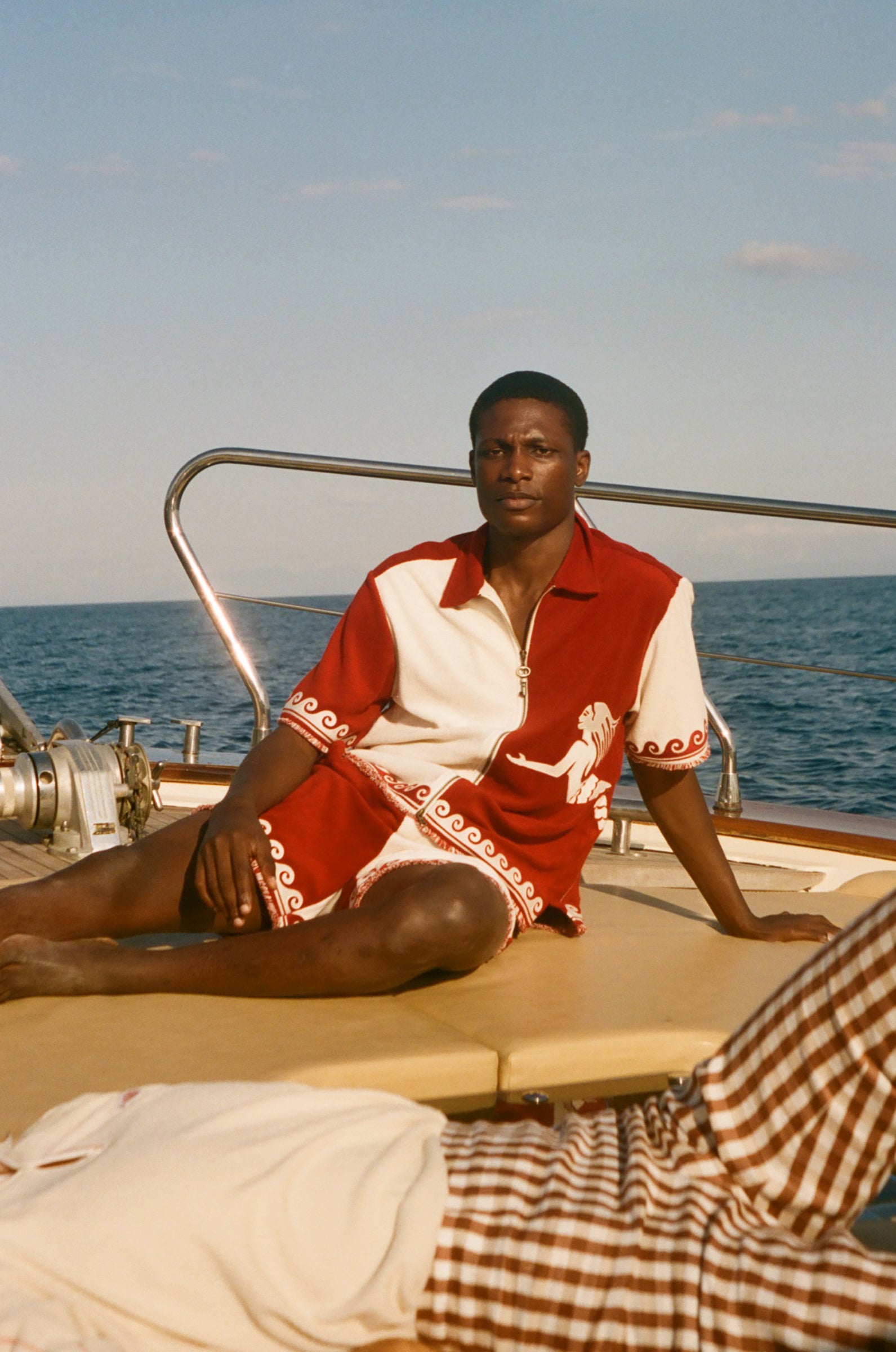Person sitting on a boat wearing a red and white outfit with ocean and sky in the background