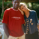 Two people standing close together outdoors with a red shirt featuring 'Le Sireneuse' branding.