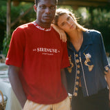 Two people standing close together outdoors with a red shirt featuring 'Le Sireneuse' branding.