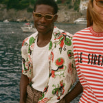 Man wearing a colorful shirt and sunglasses with a scenic coastal background