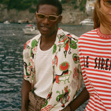 Man wearing a colorful shirt and sunglasses with a scenic coastal background