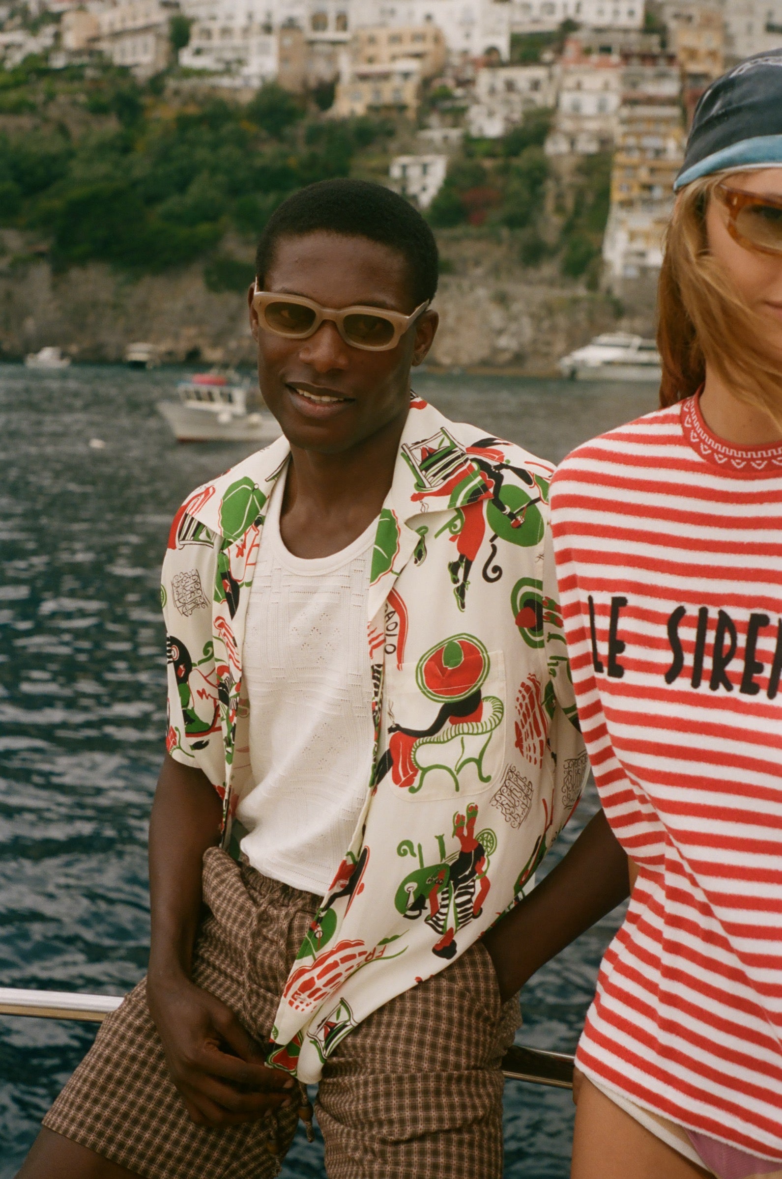 Man wearing a colorful shirt and sunglasses with a scenic coastal background