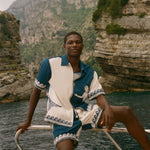 Man wearing Le Sirenuse Late Checkout Cabana, sitting on the edge of a boat.