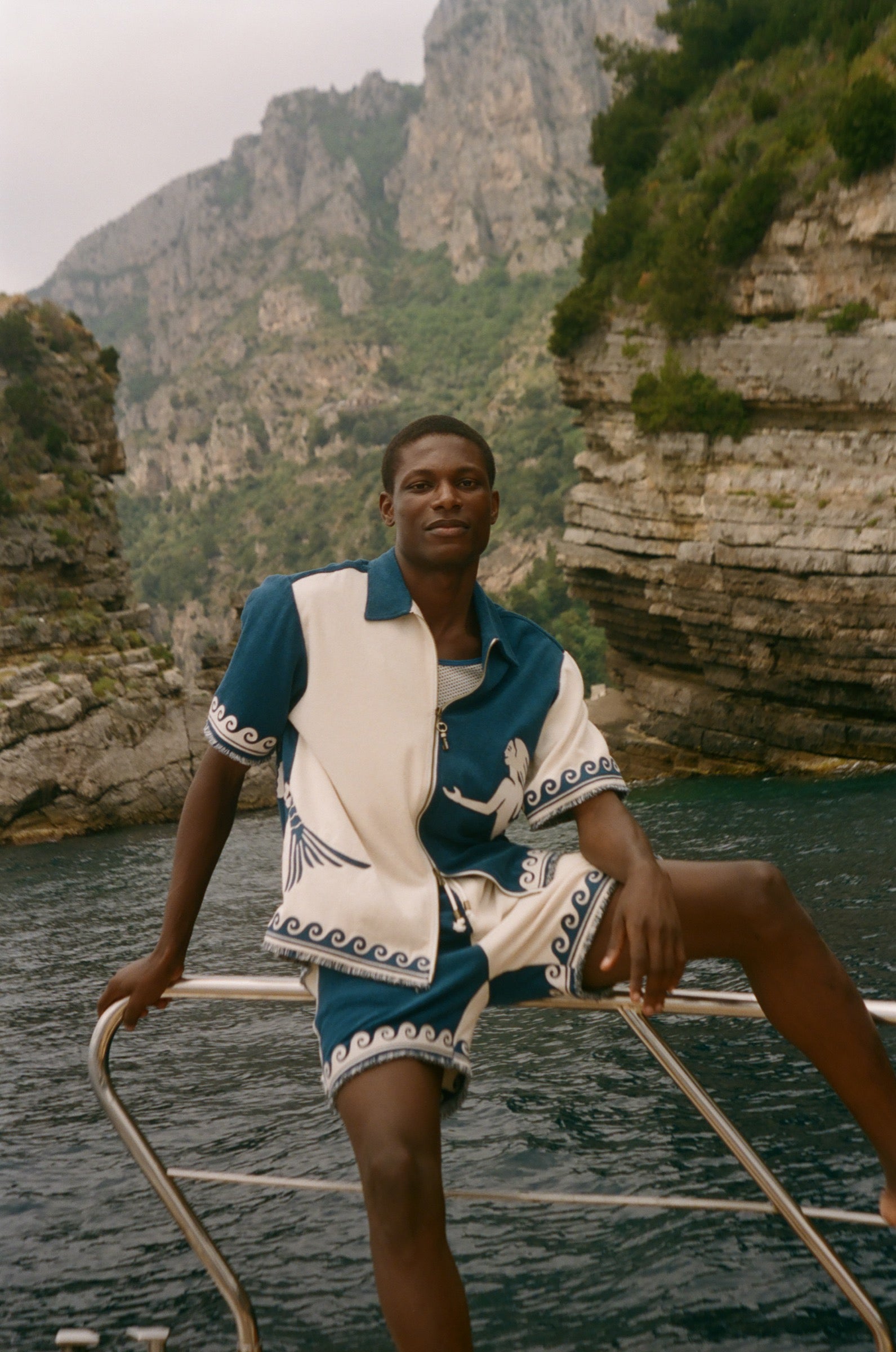 Man wearing Le Sirenuse Late Checkout Cabana, sitting on the edge of a boat.