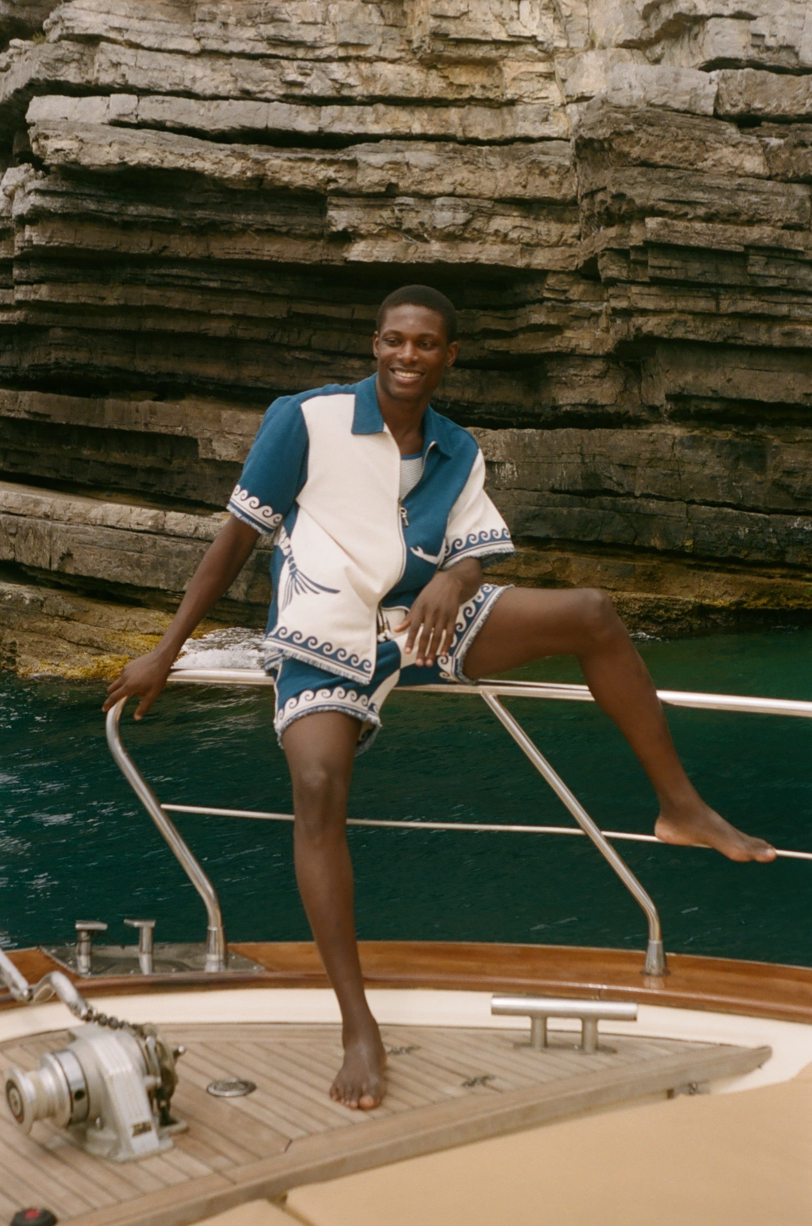 Man sitting on the edge of a boat, wearing the blue Late Checkout Cabana set. 