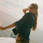 Woman on a boat wearing a dark blue top and patterned shorts with sunglasses.