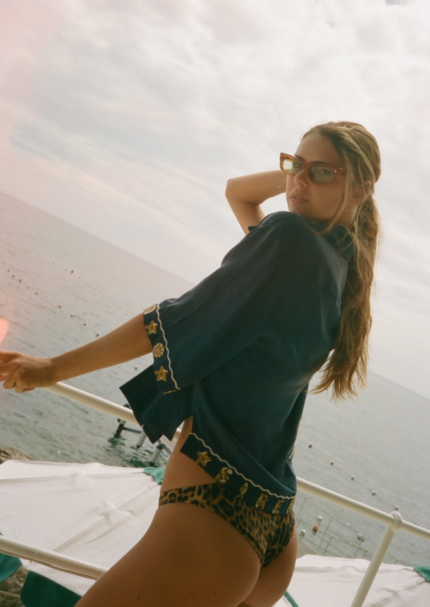 Woman on a boat wearing a dark blue top and patterned shorts with sunglasses.