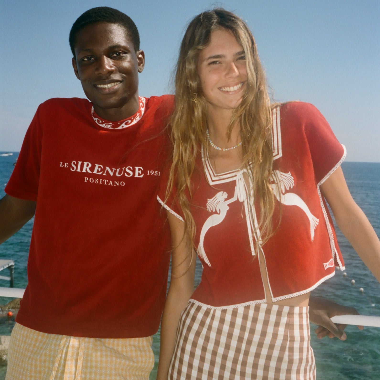Two people wearing Le Sirenuse merchandise, standing by the ocean. 
