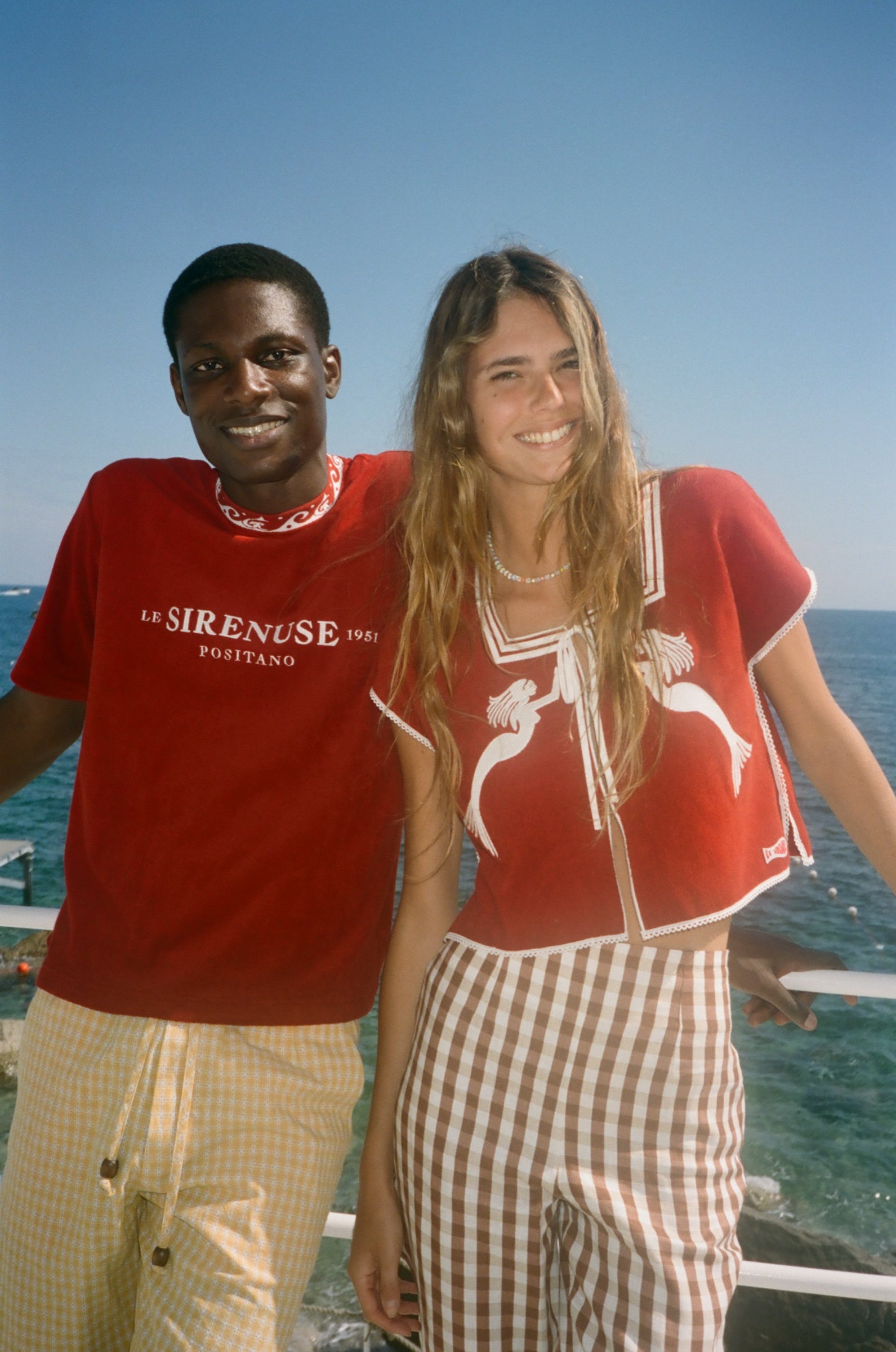 Two people wearing Le Sirenuse merchandise, standing by the ocean. 