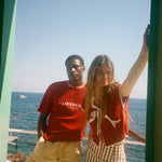 Two people standing by a scenic ocean view with a green frame, wearing shirts from the Le Sirenuse x Tombolo collaboration.