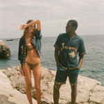 Two people wearing matching blue outfits with gold embroidery on a rocky surface.