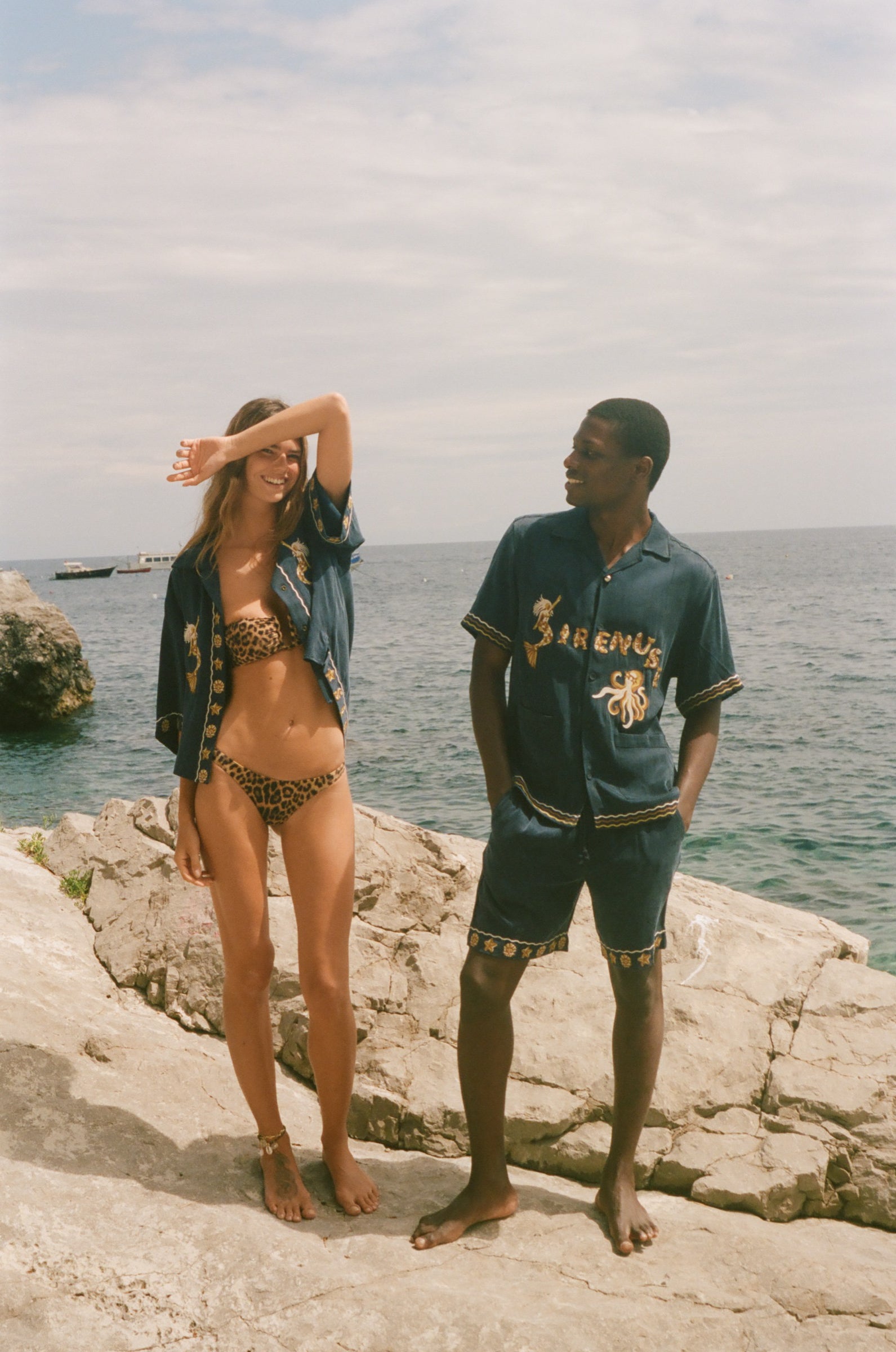 Two people wearing matching blue outfits with gold embroidery on a rocky surface.