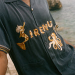 Navy blue shirt with gold embroidery on a blurred beach background