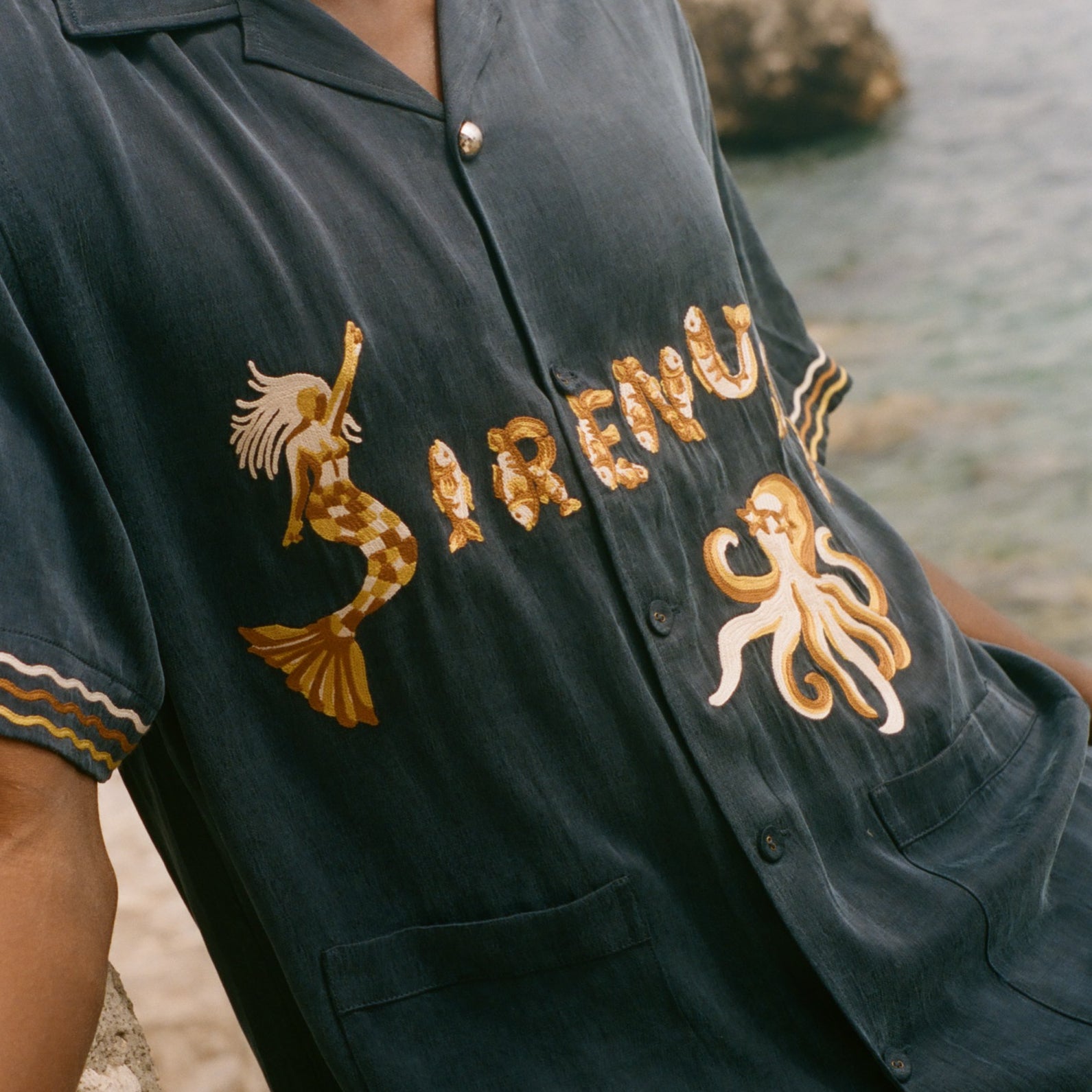 Navy blue shirt with gold embroidery on a blurred beach background