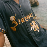 Navy blue shirt with gold embroidery on a blurred beach background
