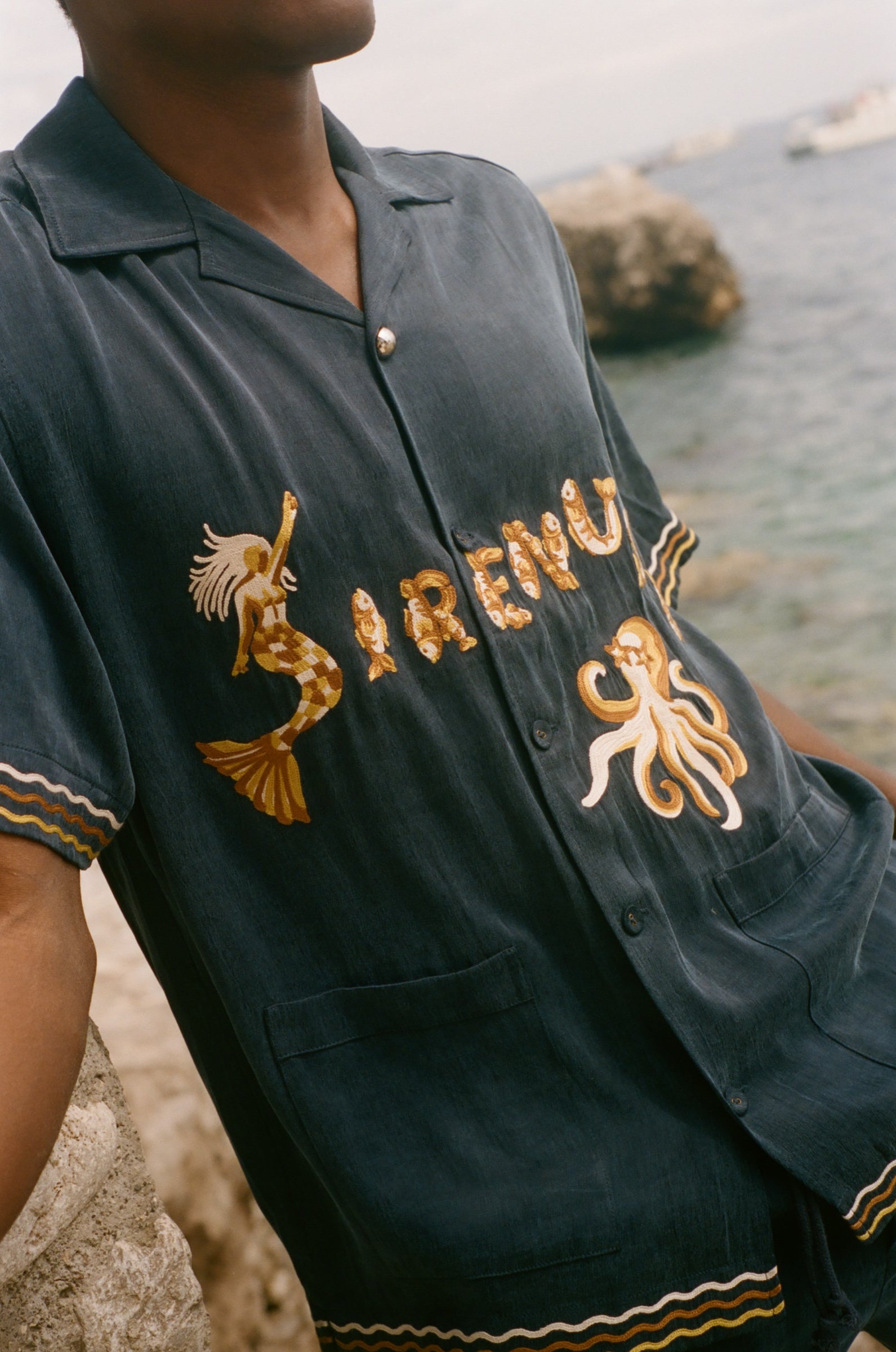 Navy blue shirt with gold embroidery on a blurred beach background